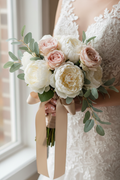 Hand-tied silk bridal bouquet of ivory peonies and blush garden roses with eucalyptus held against ivory wedding dress bodice
