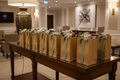 Ten kraft paper welcome bags tied with sage ribbon lined up on wooden hotel console table with treats visible at top