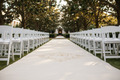 Ivory canvas aisle runner unrolling down garden courtyard aisle with white chairs and magnolia trees in golden afternoon light