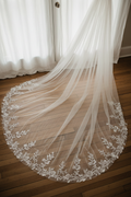 Cathedral-length ivory tulle veil draped across wooden floor with hand-embroidered floral border in soft natural light
