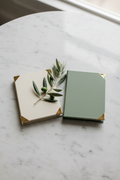 Ivory and sage hardcover vow books on marble table with olive branch sprig and gold foil corner detail